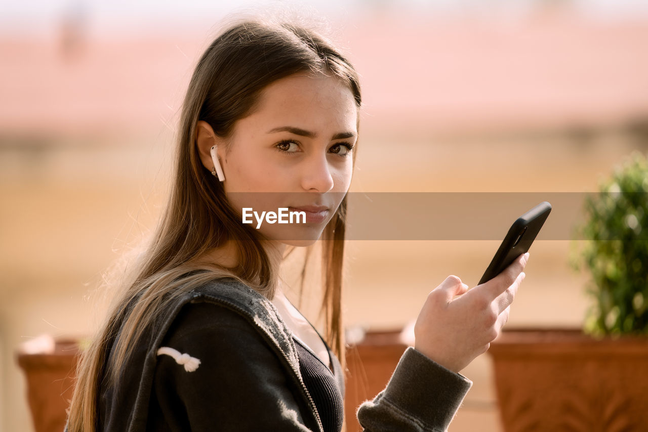 European teenager with ear buds and a smartphone. blurred background. long hair bwith a black shirt