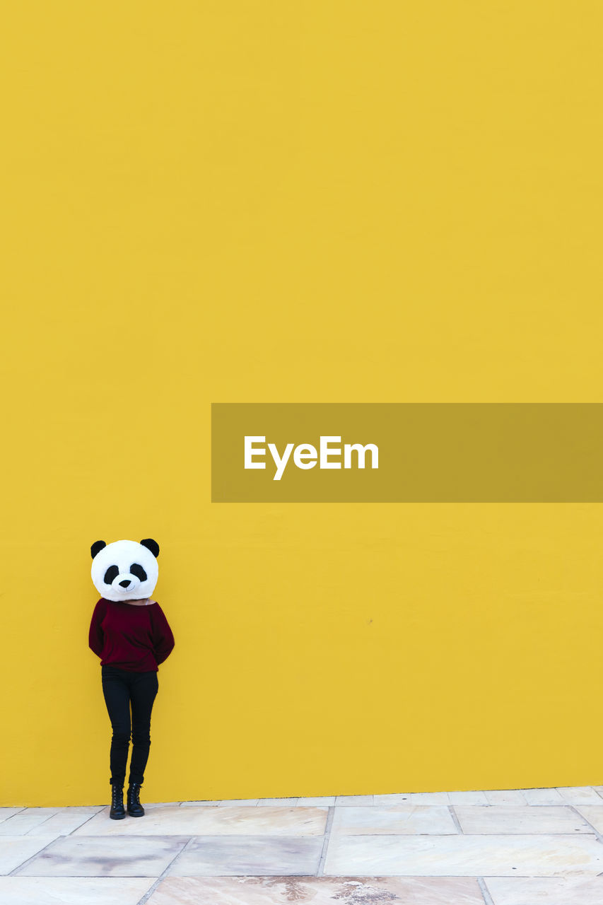 Female wearing panda mask while standing against yellow wall