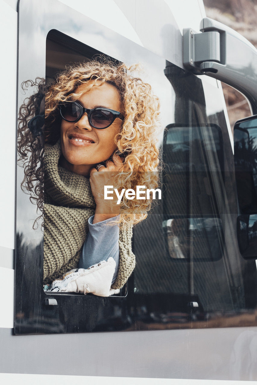 portrait of smiling young woman wearing sunglasses while standing against car