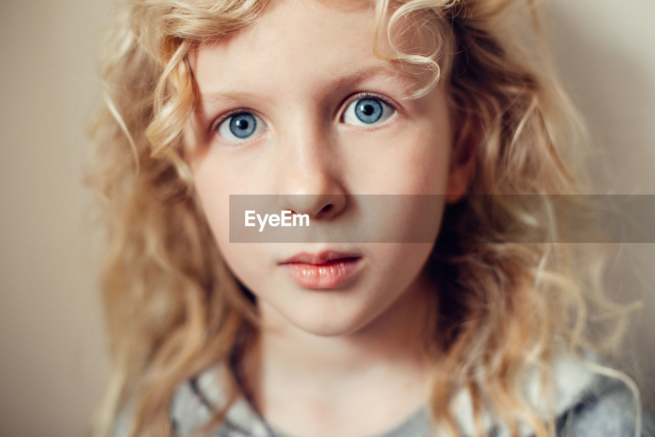 Closeup portrait of  serious caucasian blonde girl with long hair on light neutral beige background