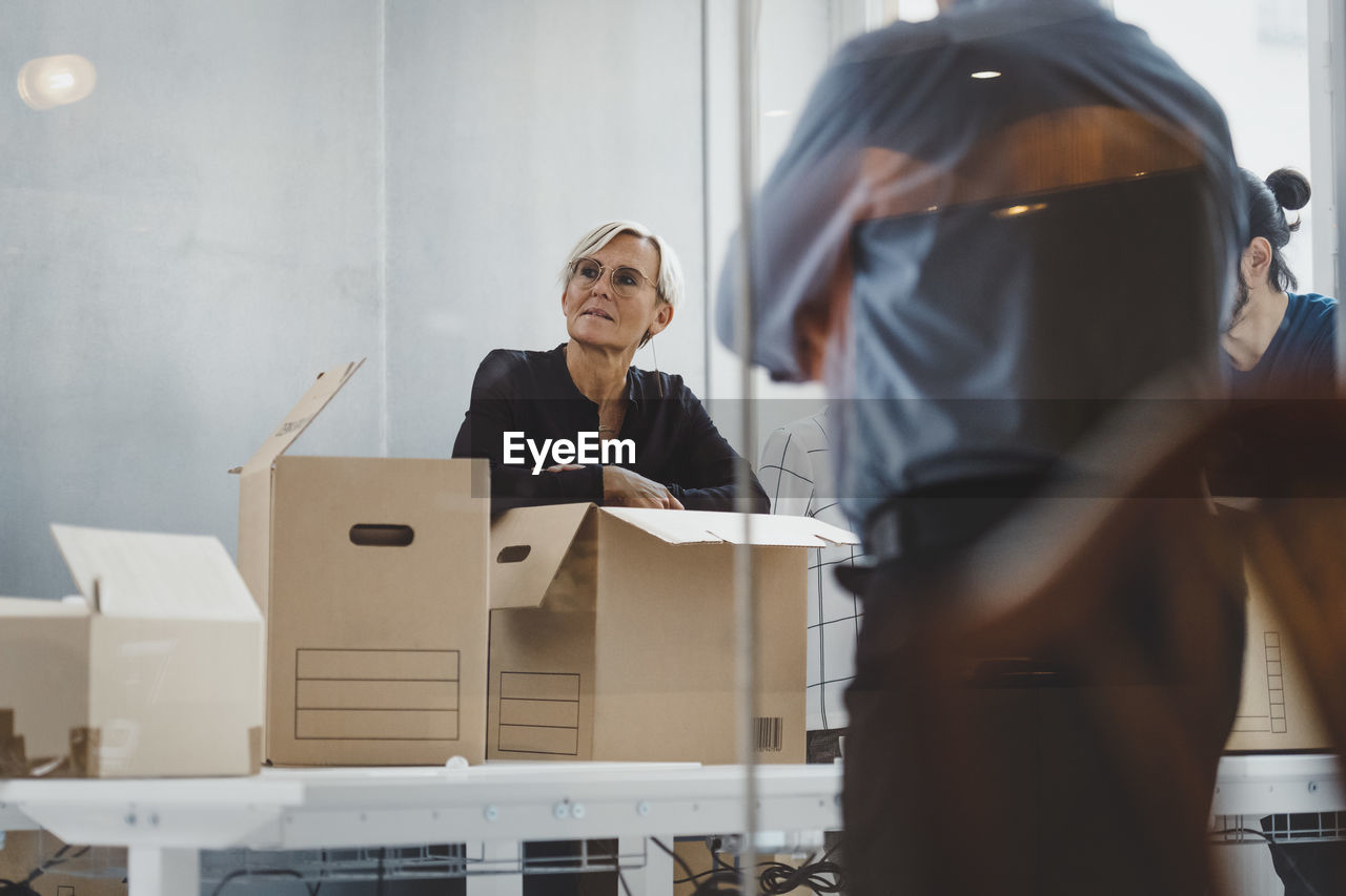 Mature businesswoman with moving boxes standing with colleagues in new office