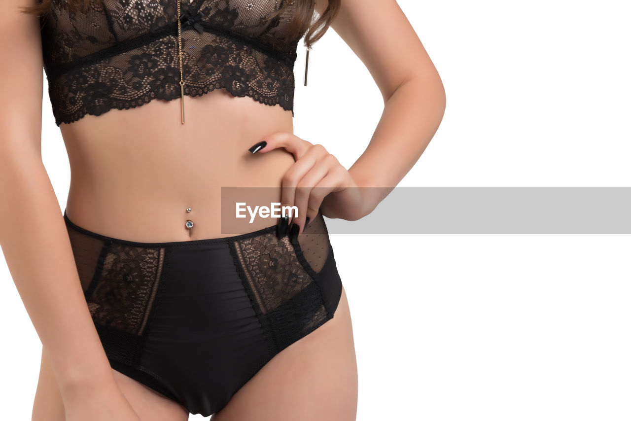 Midsection of woman in lingerie standing against white background