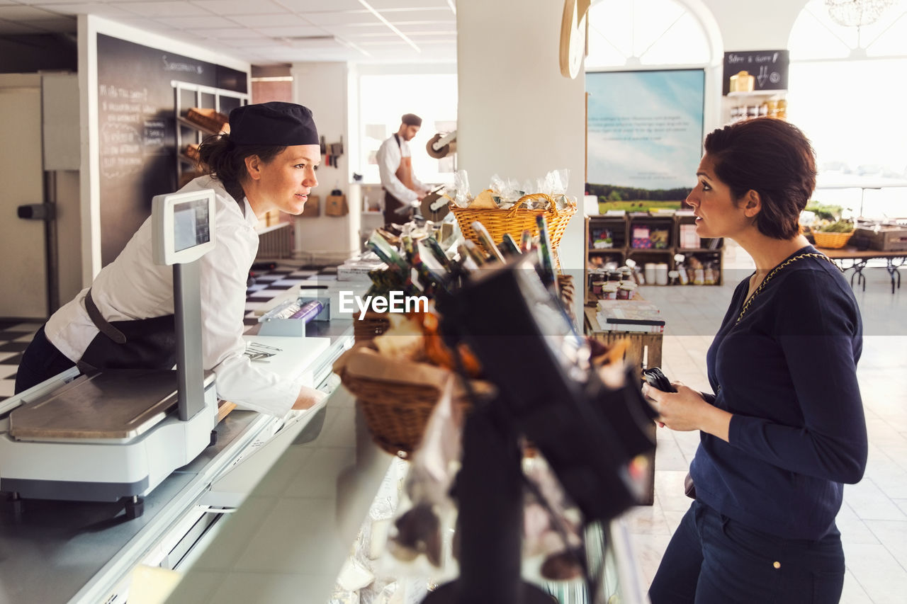 Side view of woman talking to saleswoman at counter at grocery store