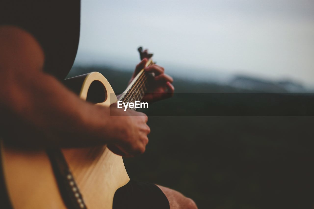 Midsection of man playing guitar against sky