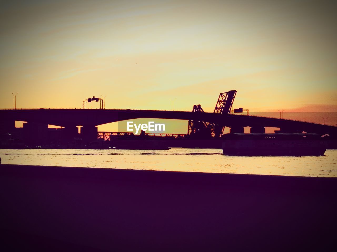 BRIDGE OVER RIVER AGAINST SKY DURING SUNSET