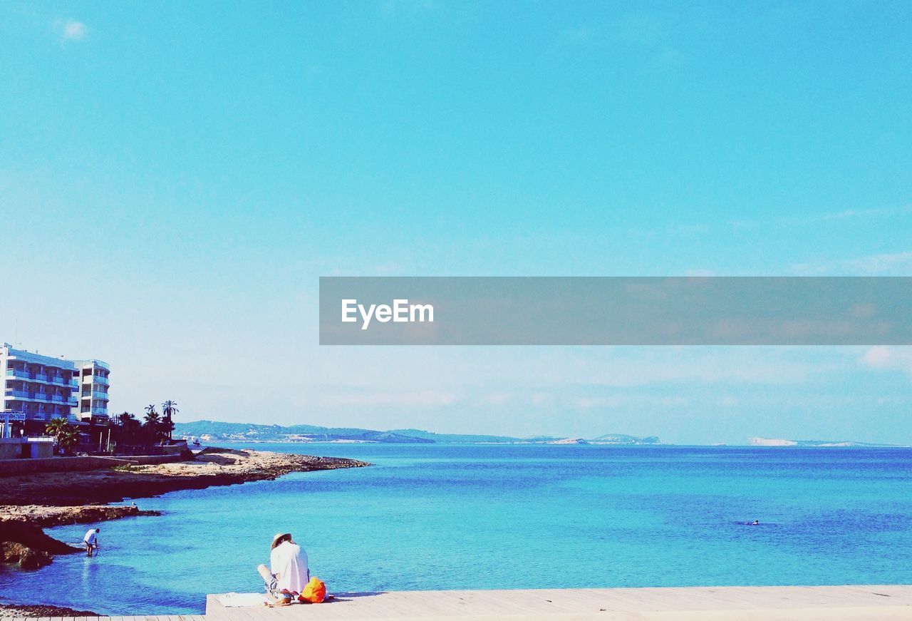 Man sitting on pier with blue sea in background