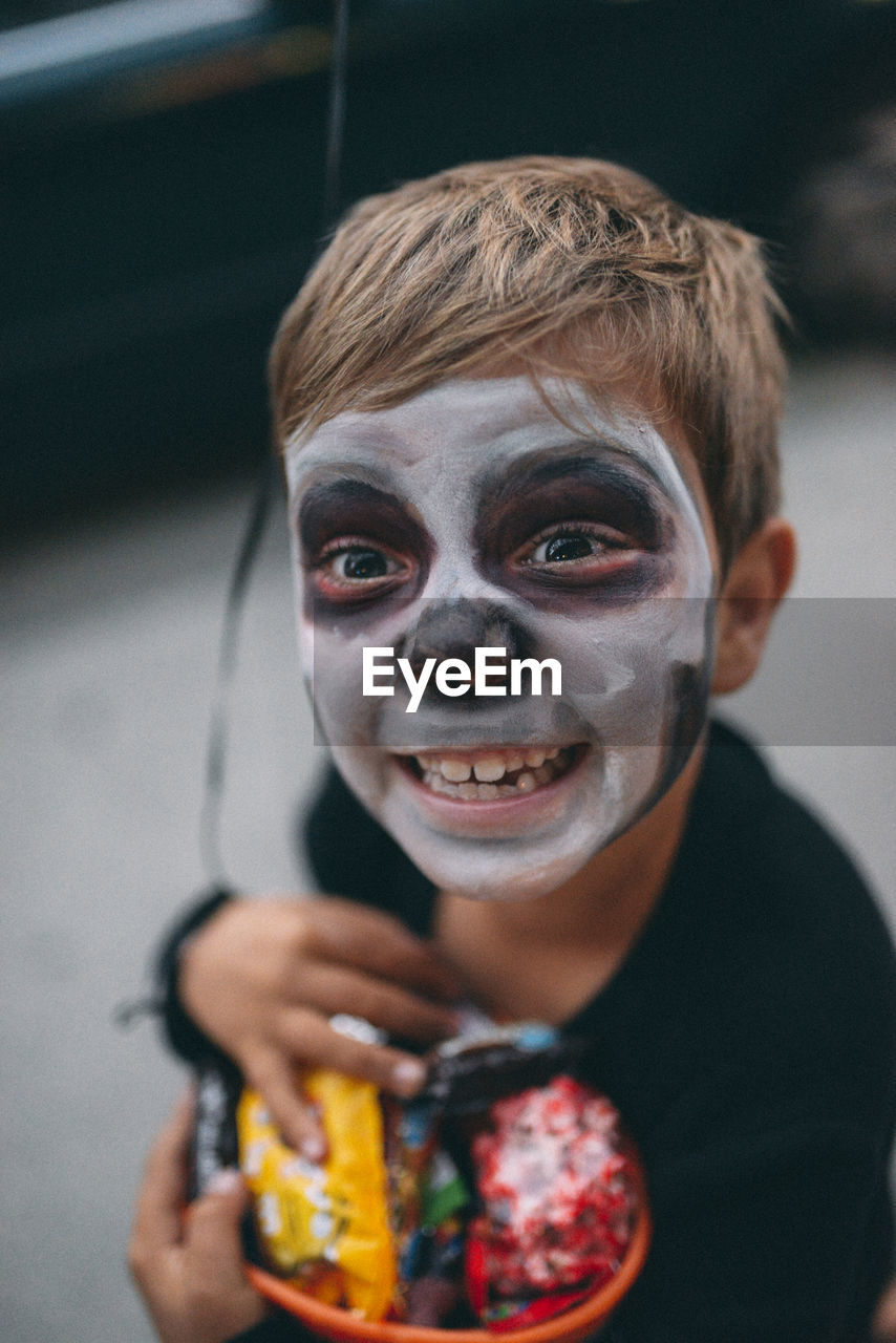 High angle view of boy with face paint holding candies during halloween