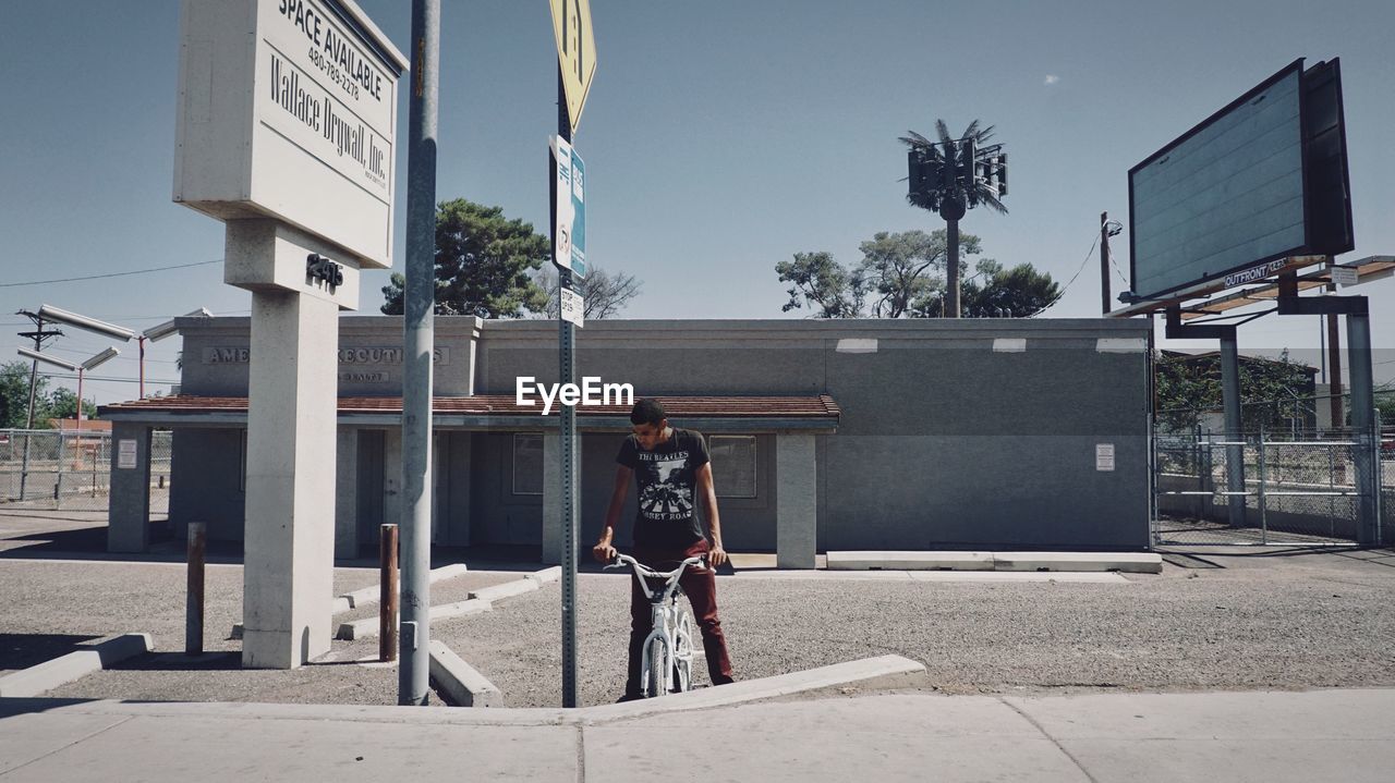 MAN STANDING BY STREET AGAINST SKY