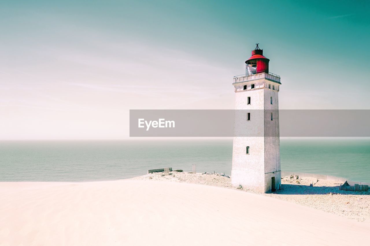 Lighthouse on beach by sea against sky