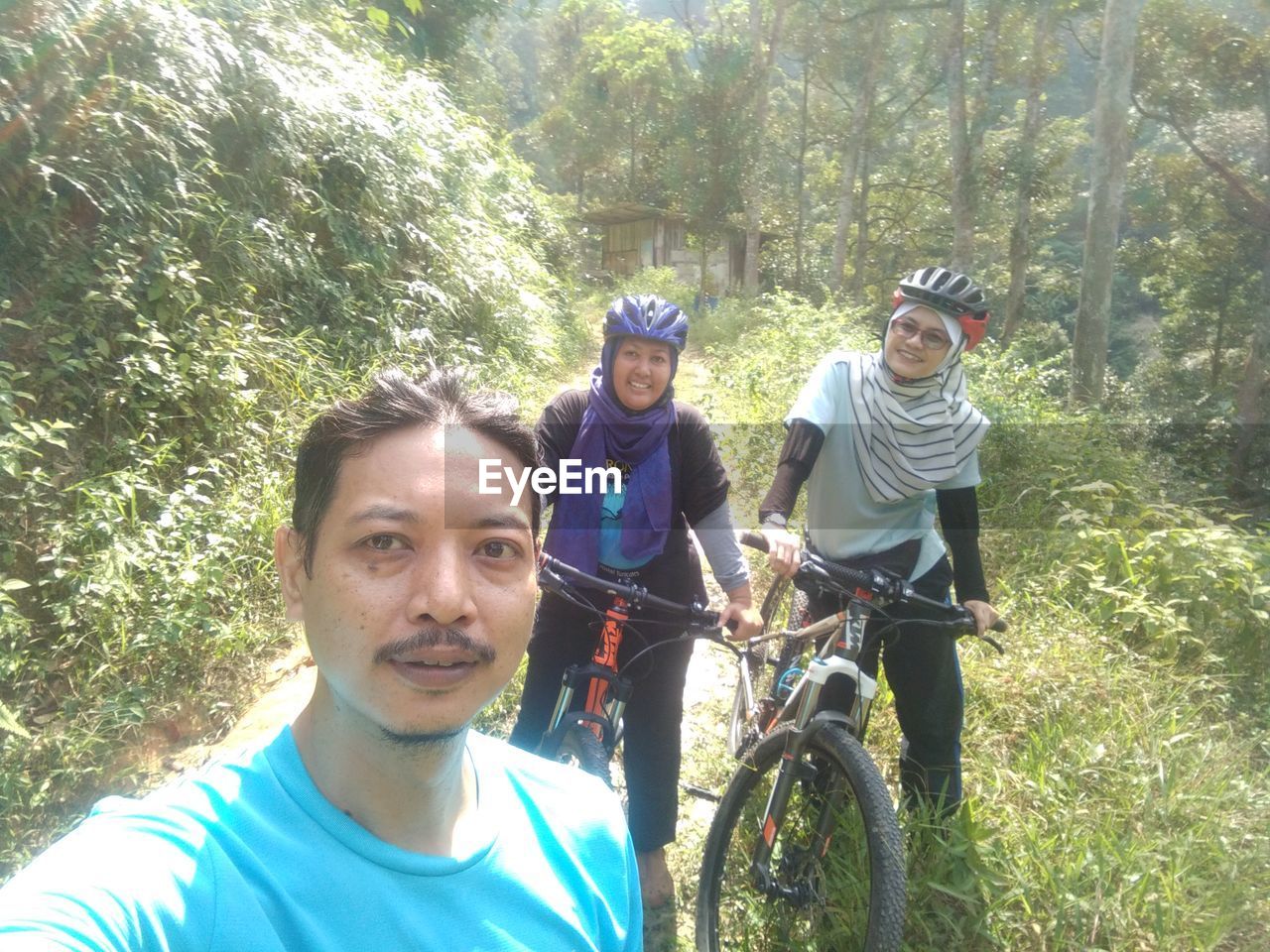 PORTRAIT OF SMILING YOUNG MAN RIDING BICYCLE ON FOREST