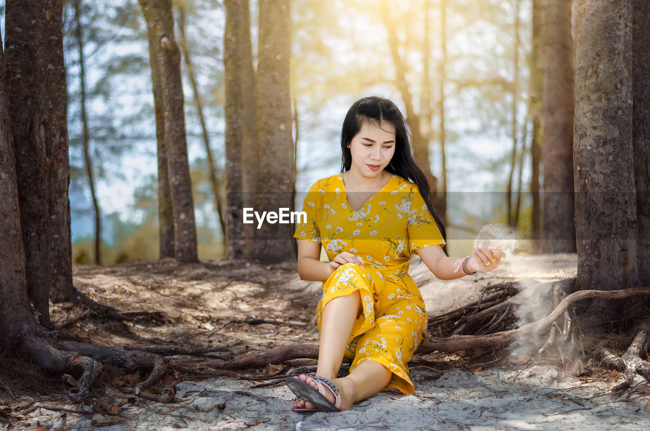 Smiling woman throwing sand while sitting on tree trunk