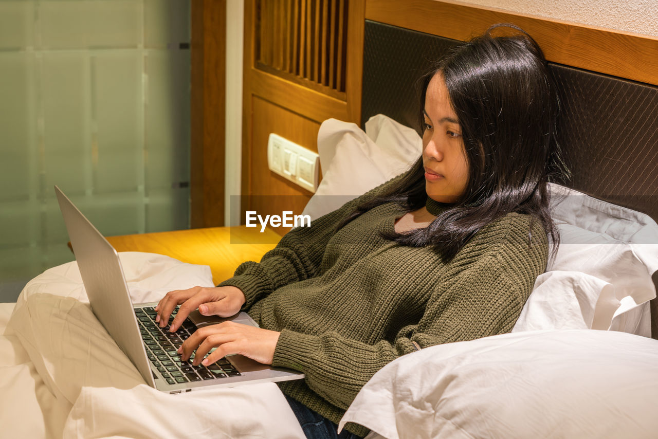 Businesswoman using laptop while lying down on bed
