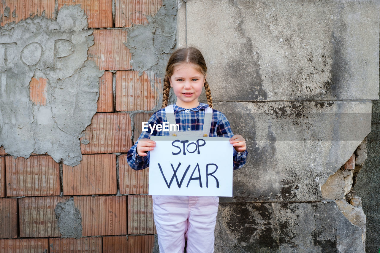 Portrait of girl holding poster against wall