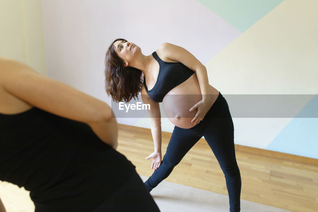 Pregnant woman stretching with instructor in yoga studio