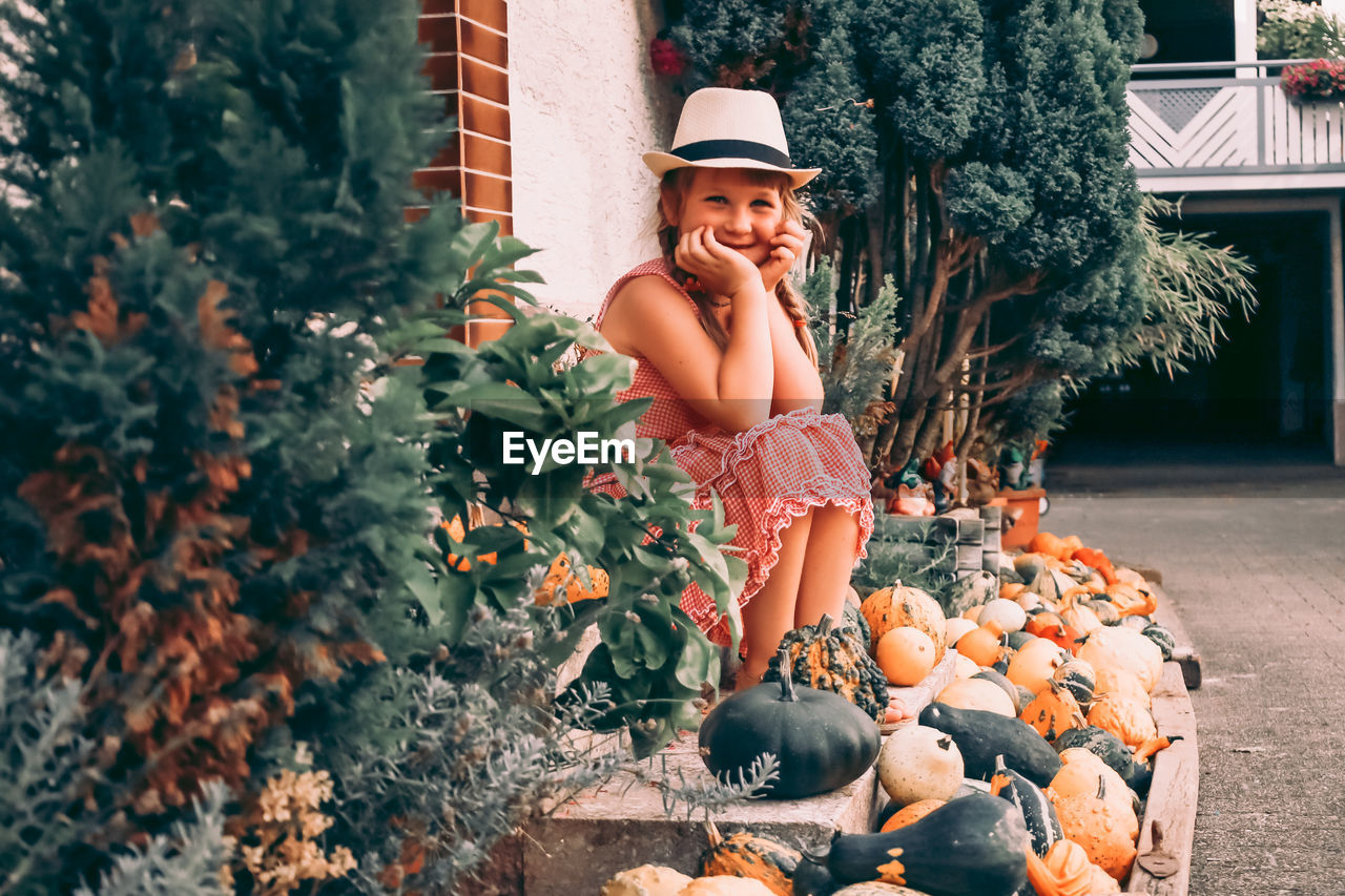 FULL LENGTH OF SMILING GIRL LOOKING AWAY WHILE STANDING BY PUMPKIN