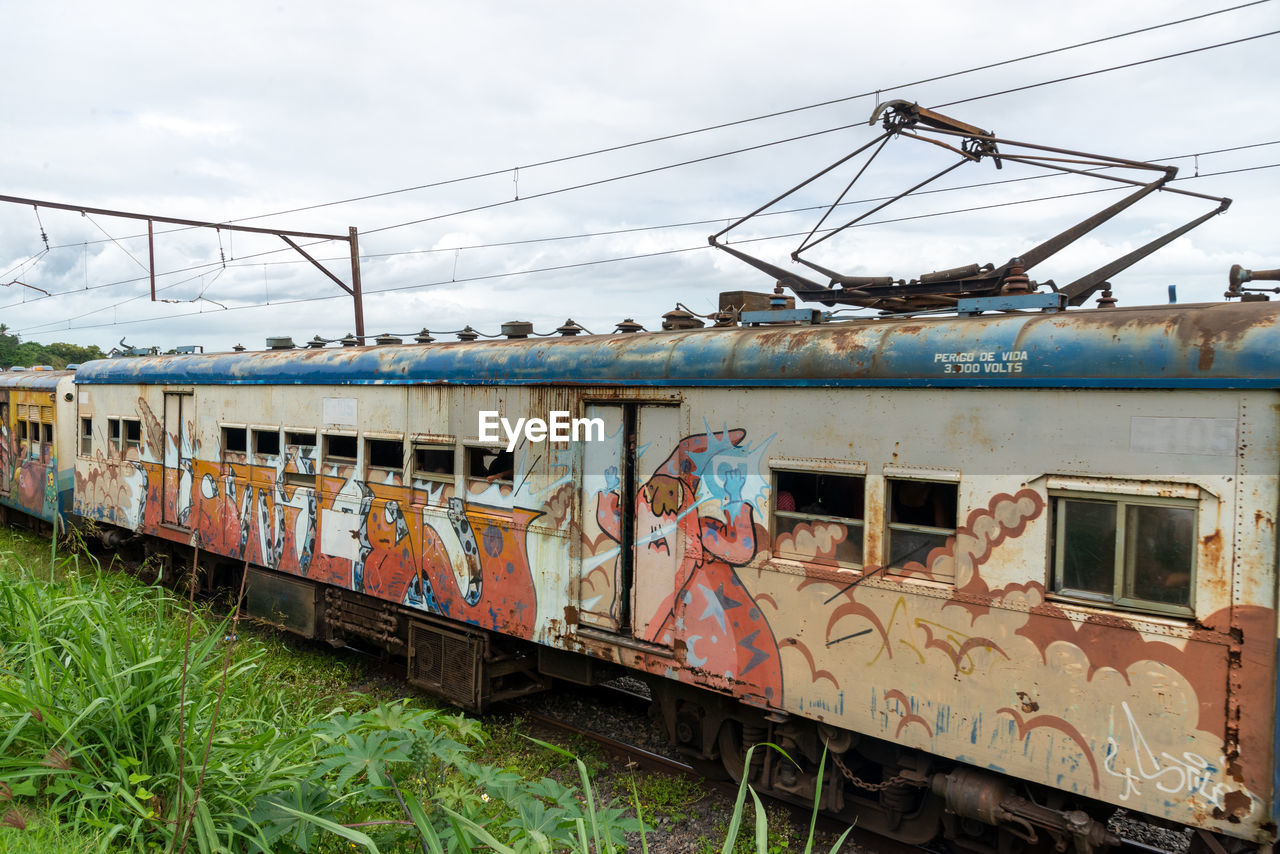 rail transportation, transport, train, mode of transportation, transportation, locomotive, railway, track, railroad track, vehicle, railroad car, rolling stock, public transportation, land vehicle, sky, nature, cloud, passenger car, travel, electricity, architecture, no people, day, grass, outdoors, metal, abandoned, rusty, old, cable, freight transportation