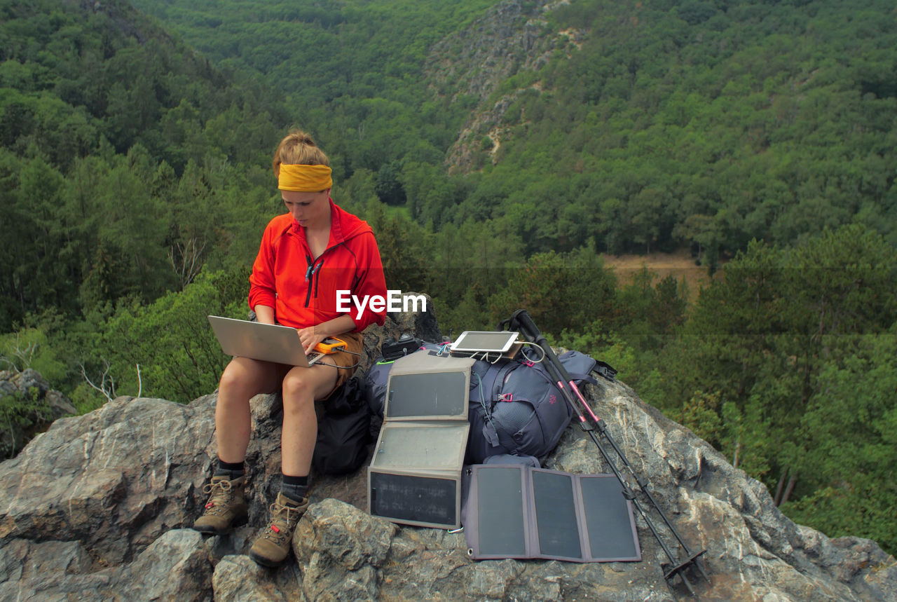 Hiker using laptop while sitting on rocky mountain