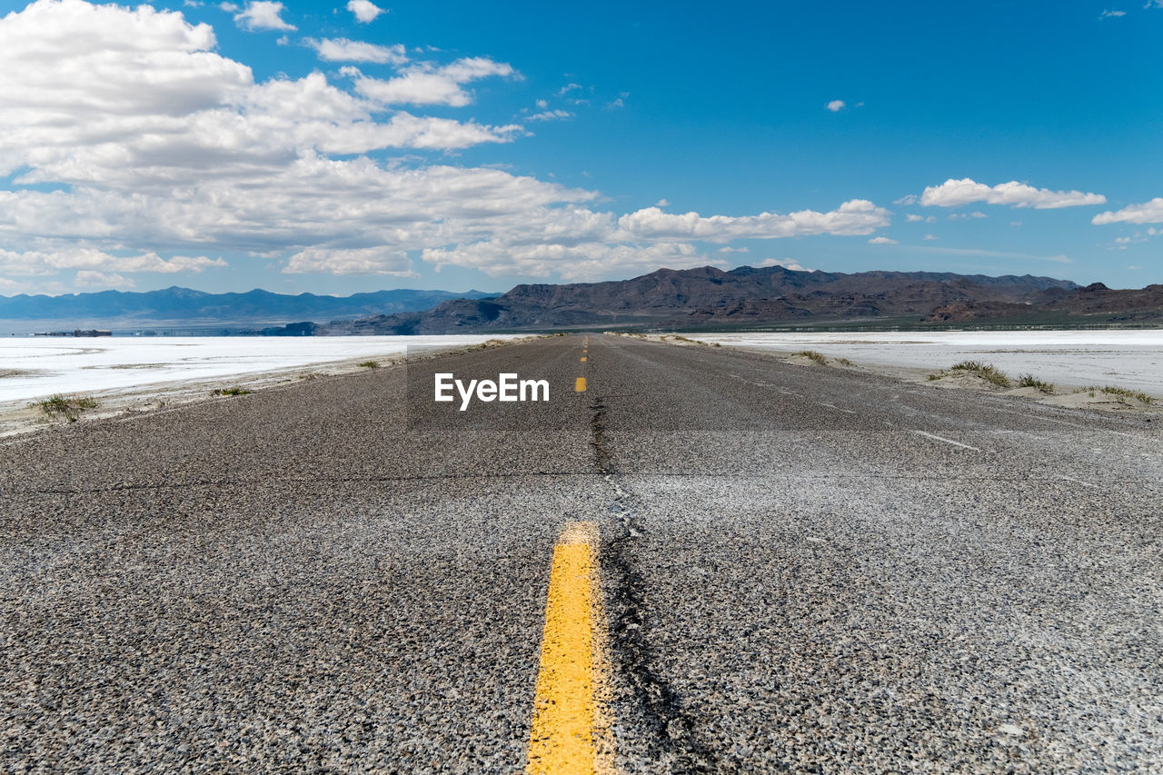 Lower angle of an empty road with some mountains on the horizon surrounded by salt flat land. 
