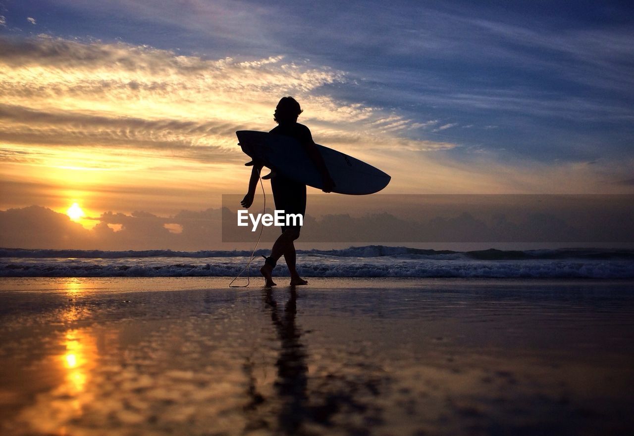 Silhouette woman with surfboard on beach at sunset