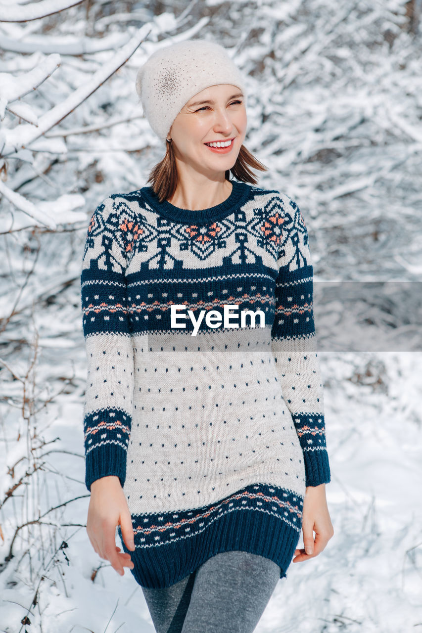 Middle age woman in woollen dress with ethnic pattern walking in park outdoor on sunny winter day