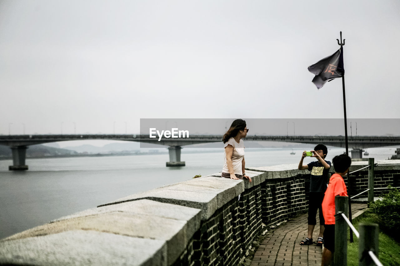 REAR VIEW OF WOMAN STANDING ON RAILING