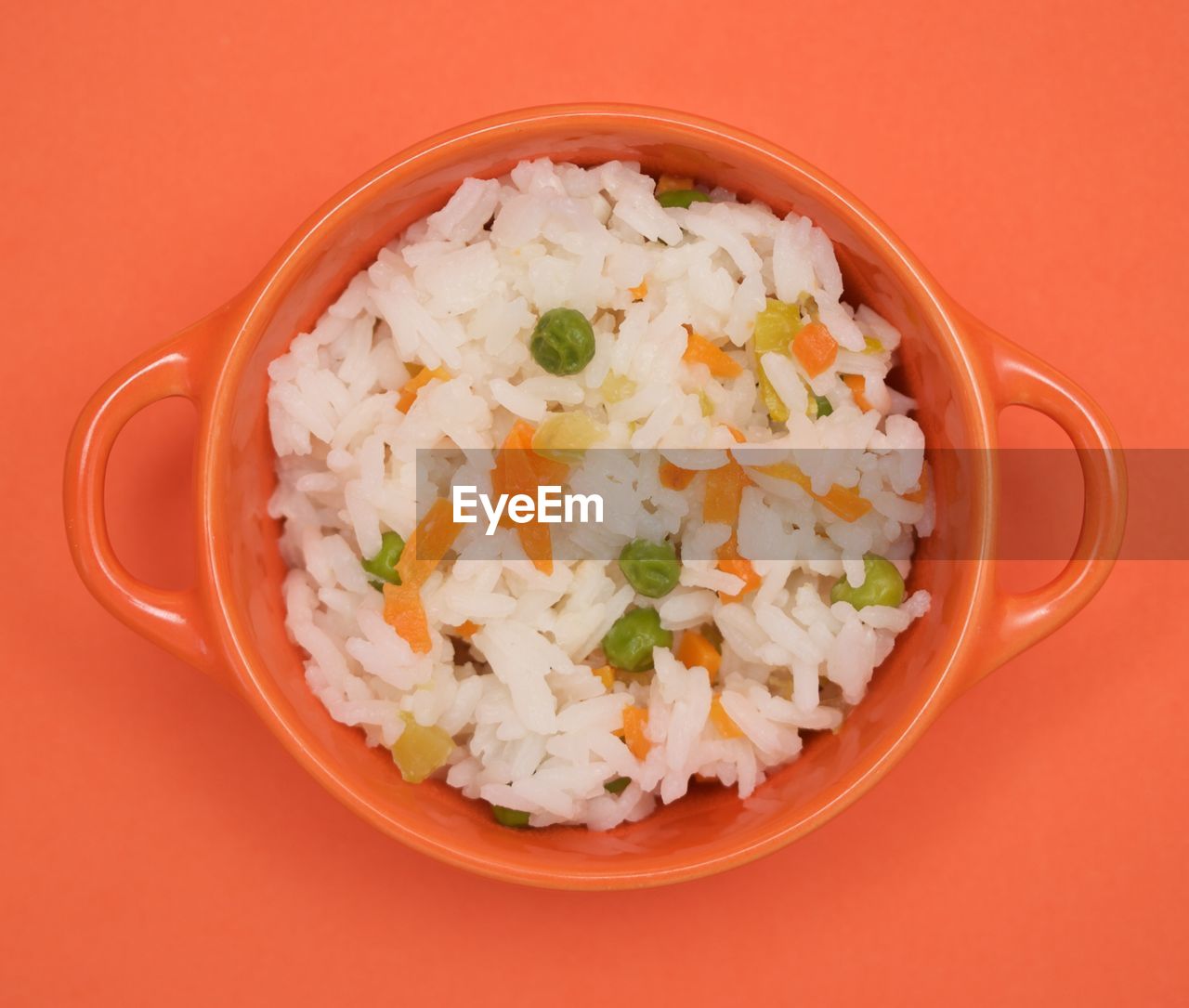 White rice, peas and carrots in an orange bowl on orange background