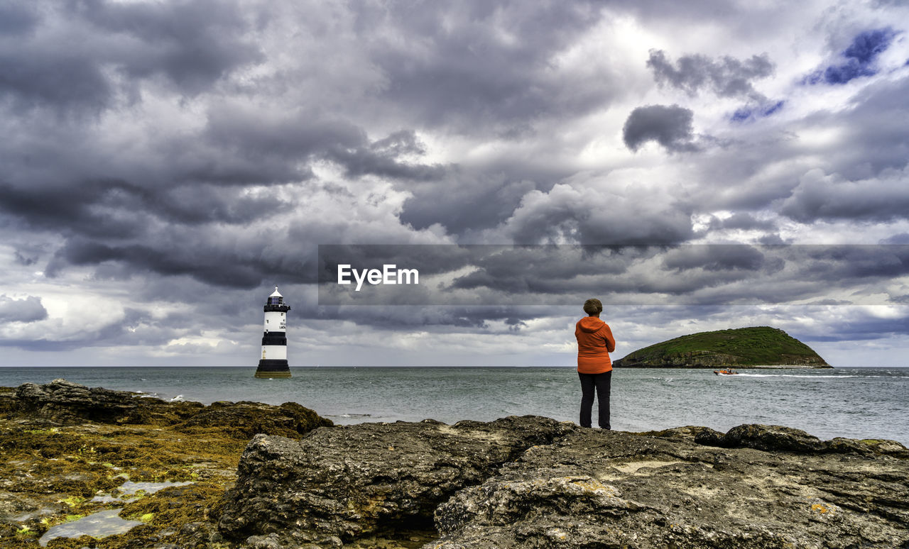 Rear view of man standing on rock by sea against sky