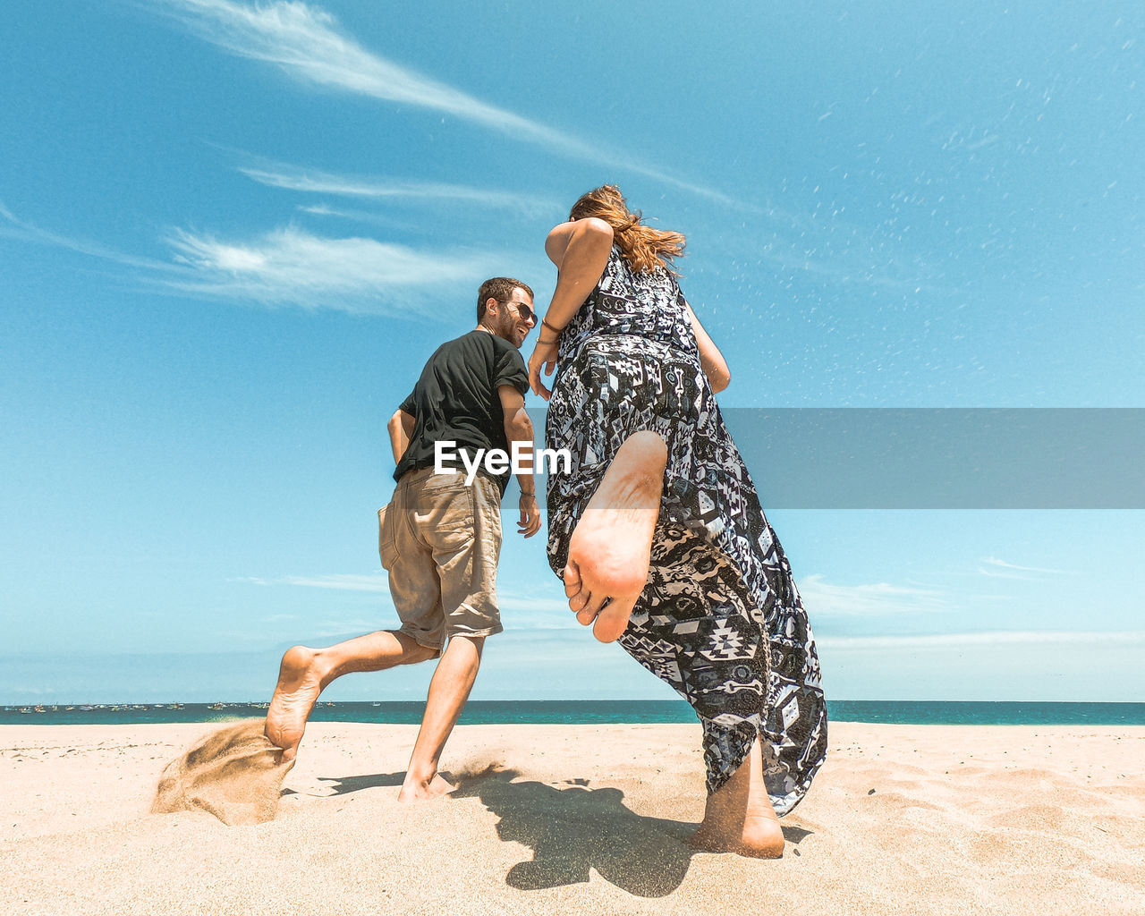 Low angle view of couple running at beach against sky