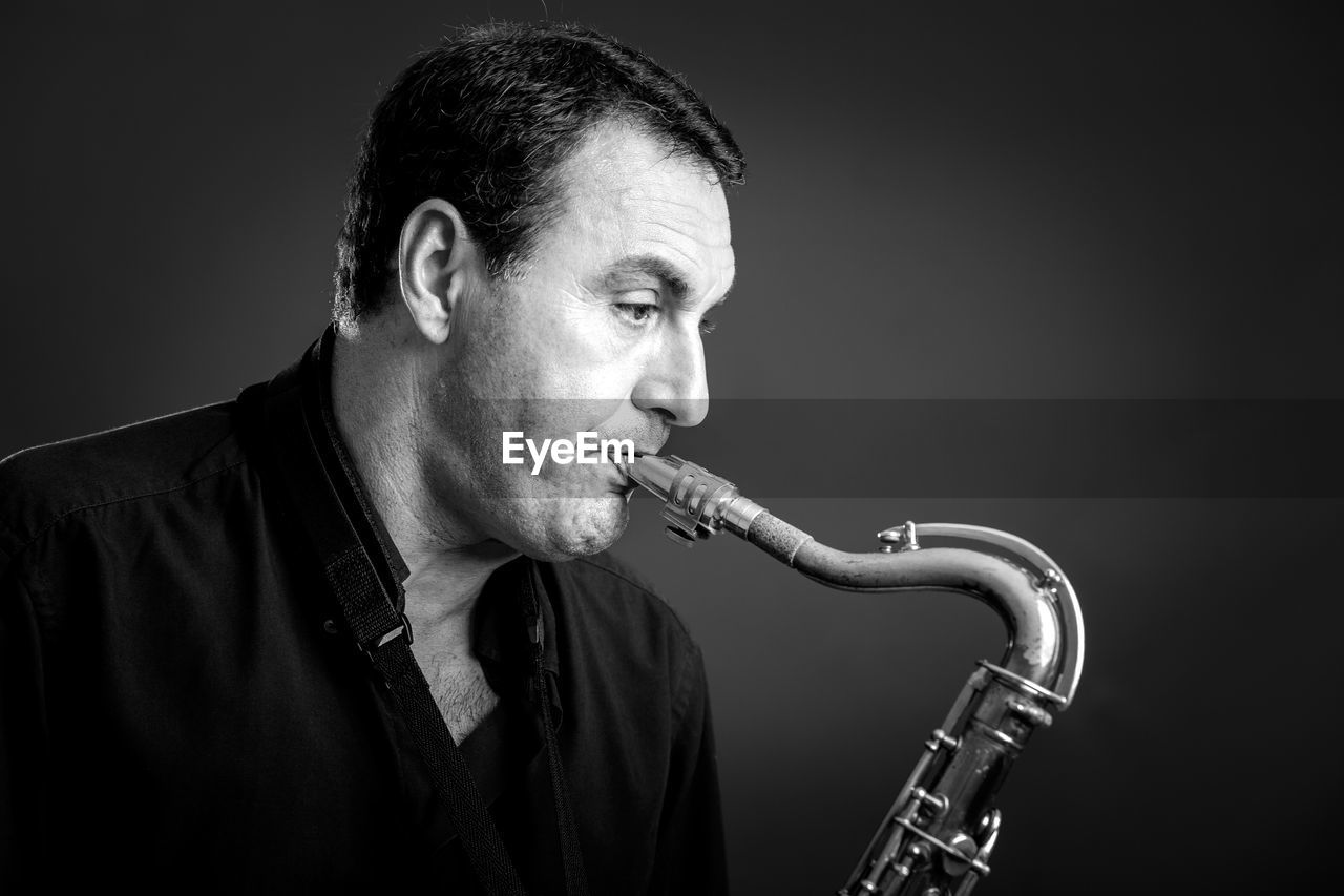 Close-up of man playing brass instrument against gray background