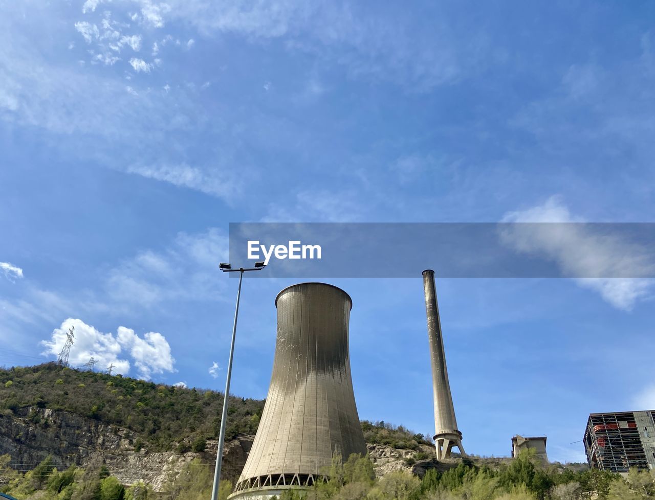 sky, cooling tower, cloud, power station, factory, industry, nuclear power plant, environment, power generation, architecture, built structure, smoke stack, nature, tower, outdoor structure, building exterior, environmental issues, wind, day, no people, pollution, outdoors, blue, landscape, plant, smoke, technology, air pollution, low angle view, social issues, environmental conservation