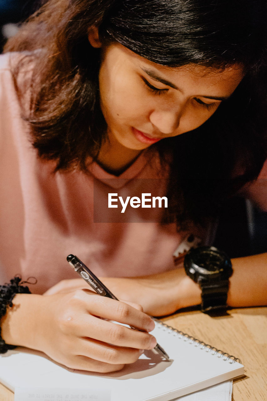 Close-up of young woman writing in book