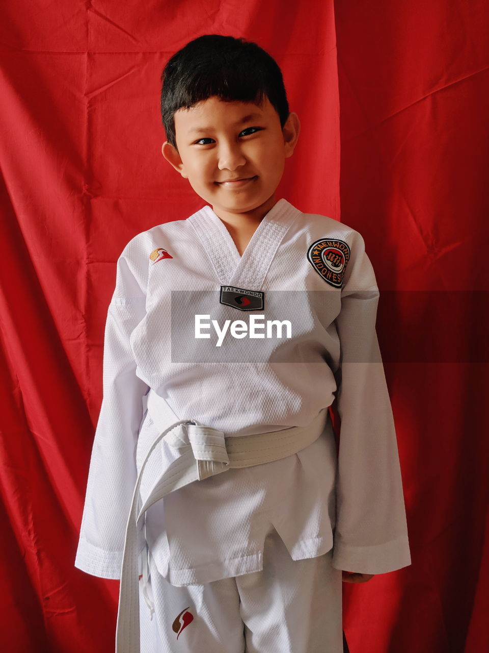 Portrait of smiling boy standing against red curtain