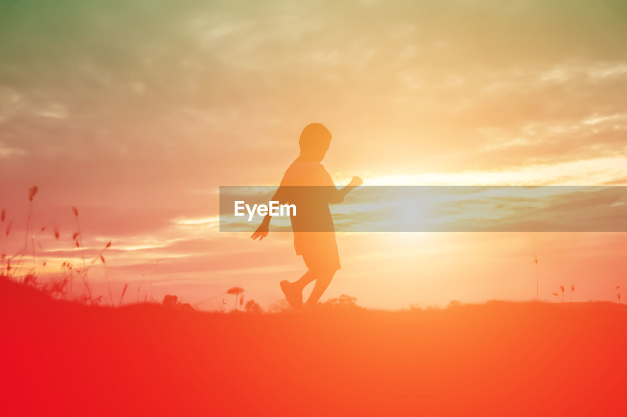 Silhouette boy dancing on land against sky during sunset