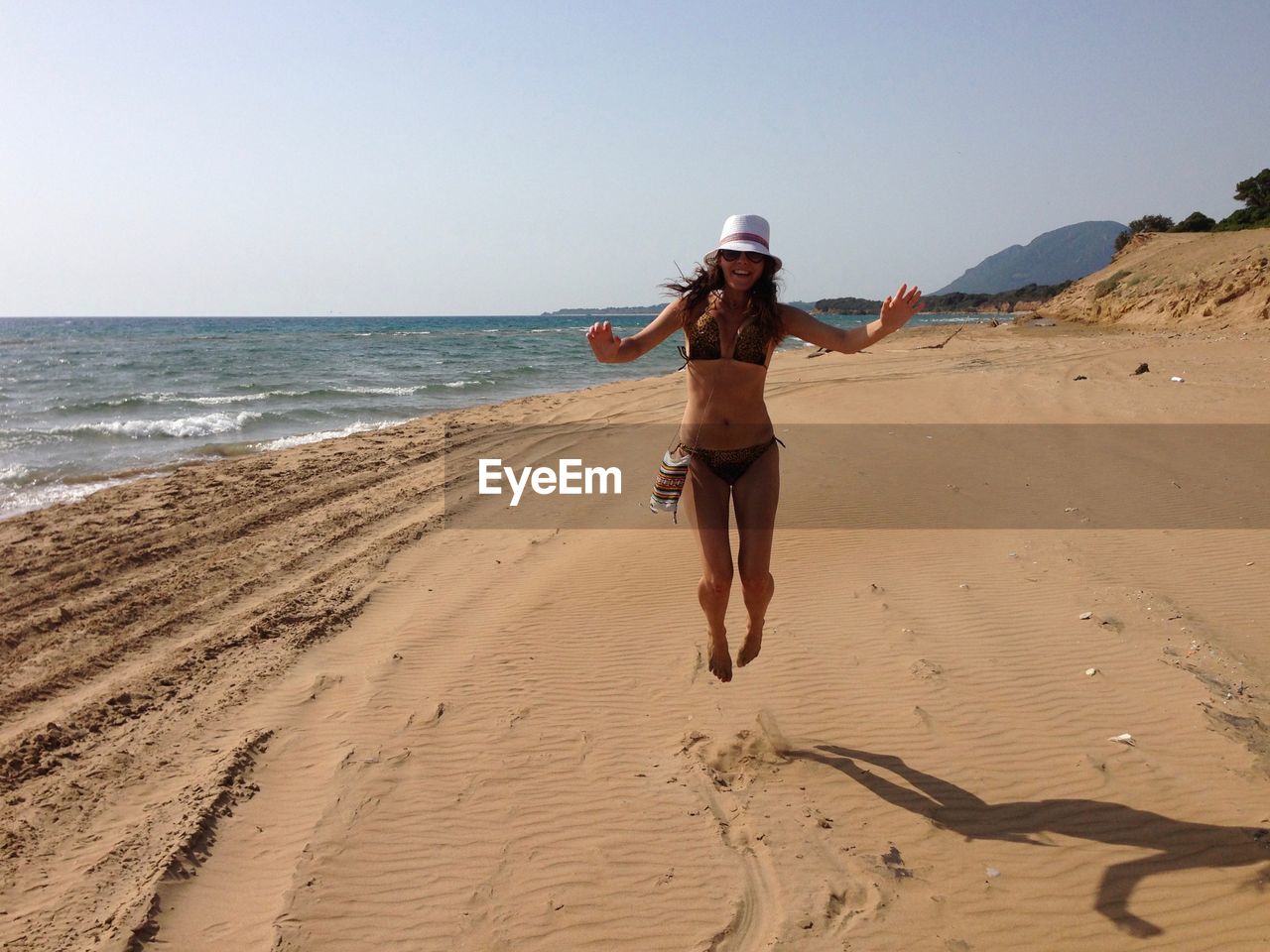 Full length of woman in bikini jumping at beach against clear sky on sunny day