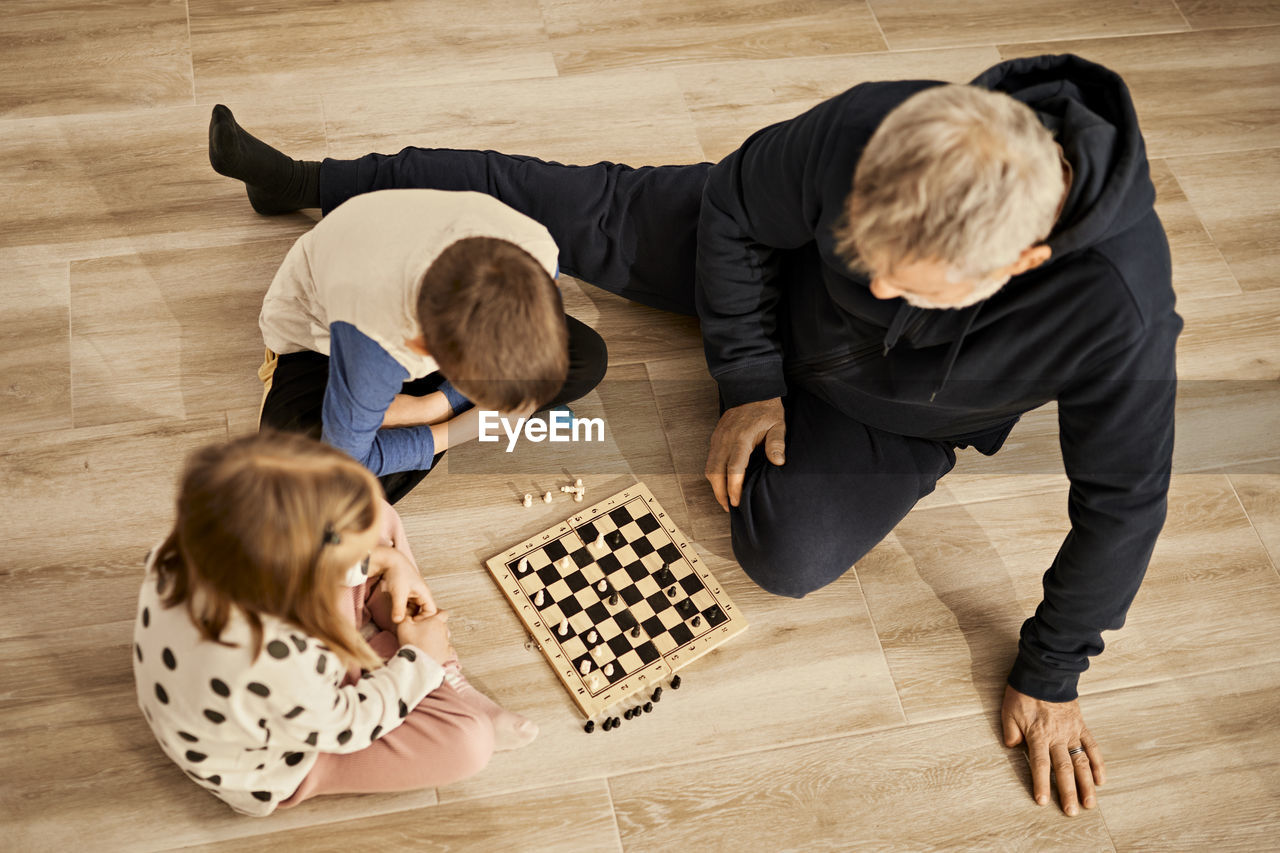 Sibling playing chess sitting with grandfather at home