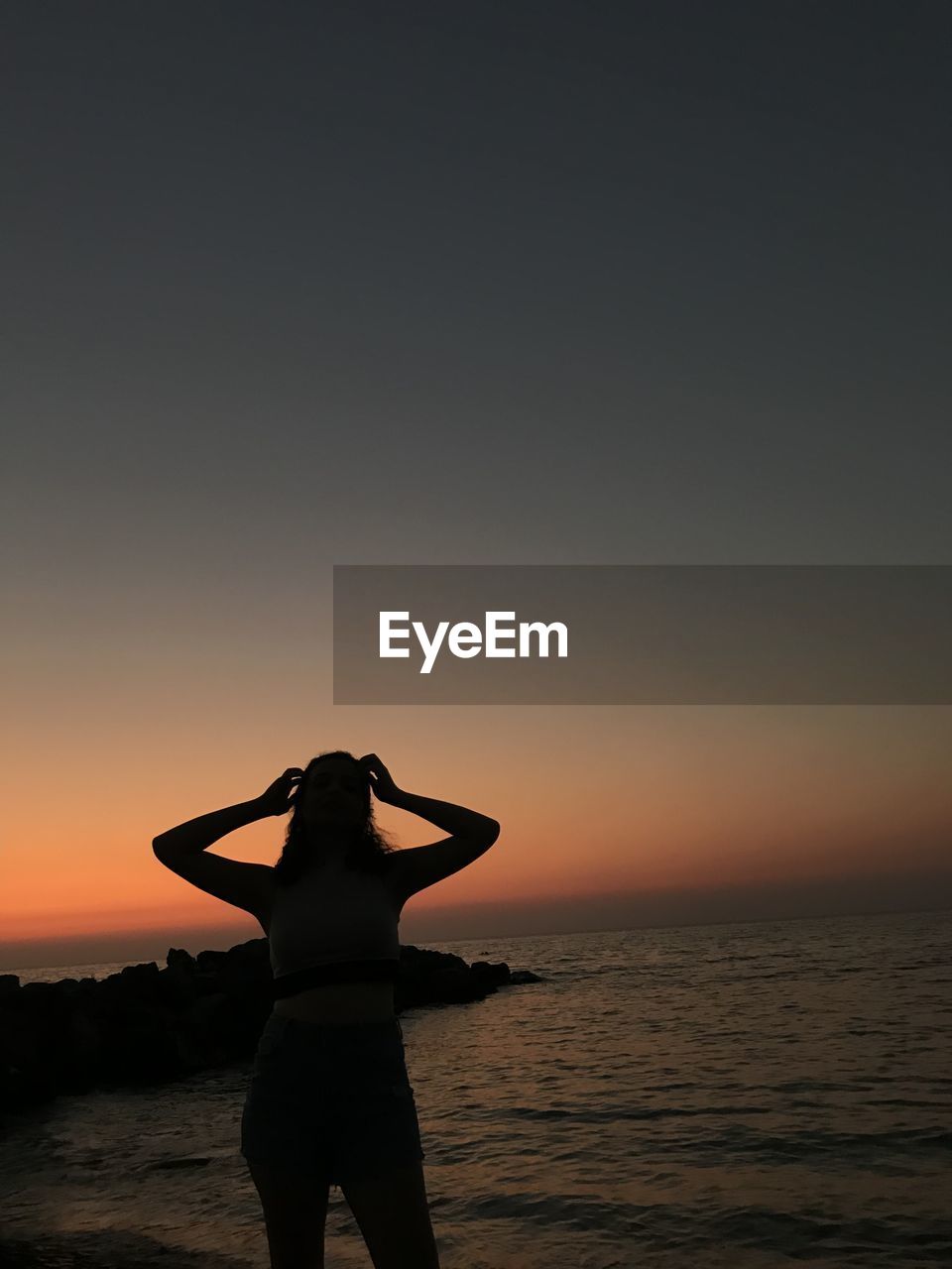 Rear view of silhouette women standing on beach during sunset
