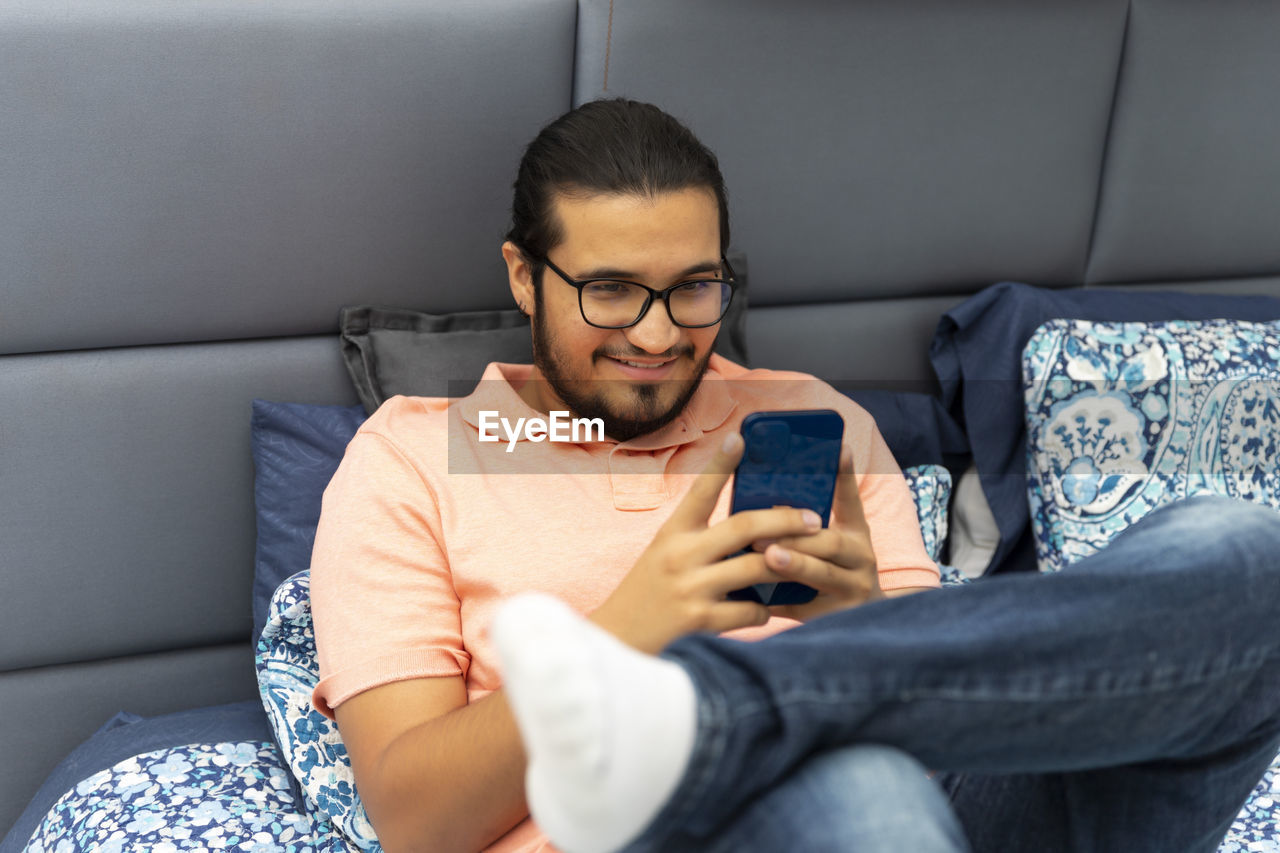 MIDSECTION OF MAN USING PHONE WHILE SITTING ON SOFA