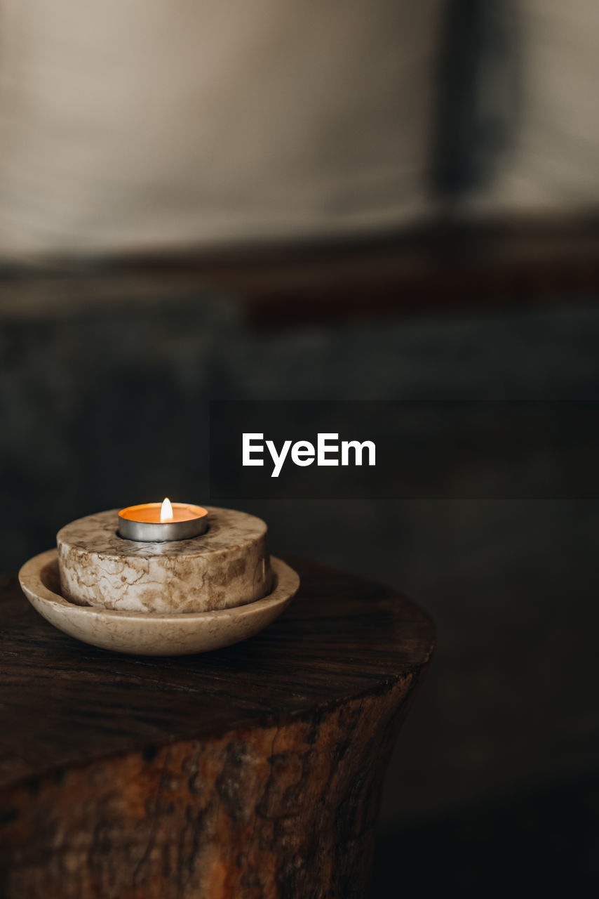 A burning candle in a marble stand on a wooden table. natural details in the interior. brown beige 