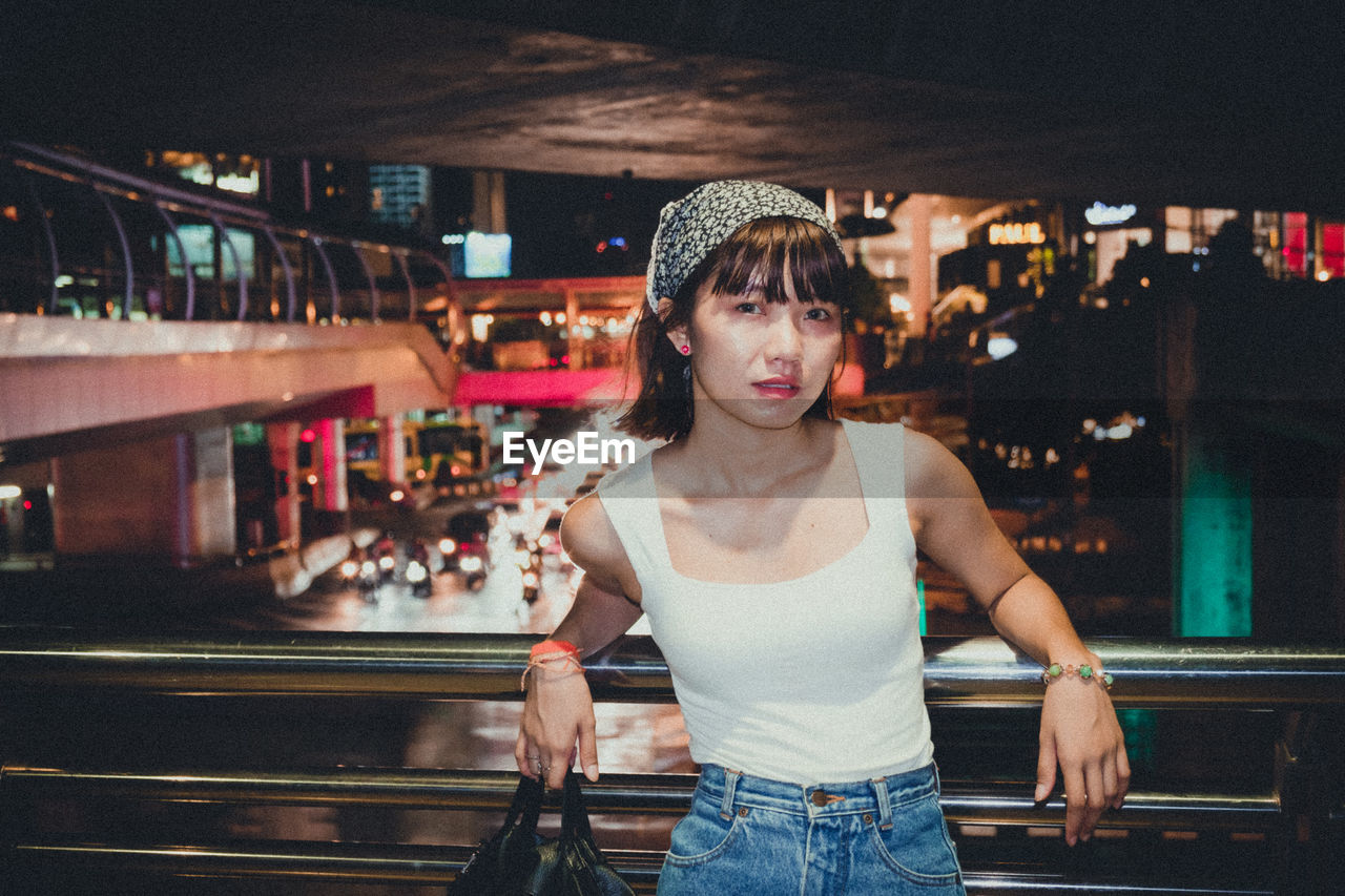 Portrait of young woman standing in footbridge at night