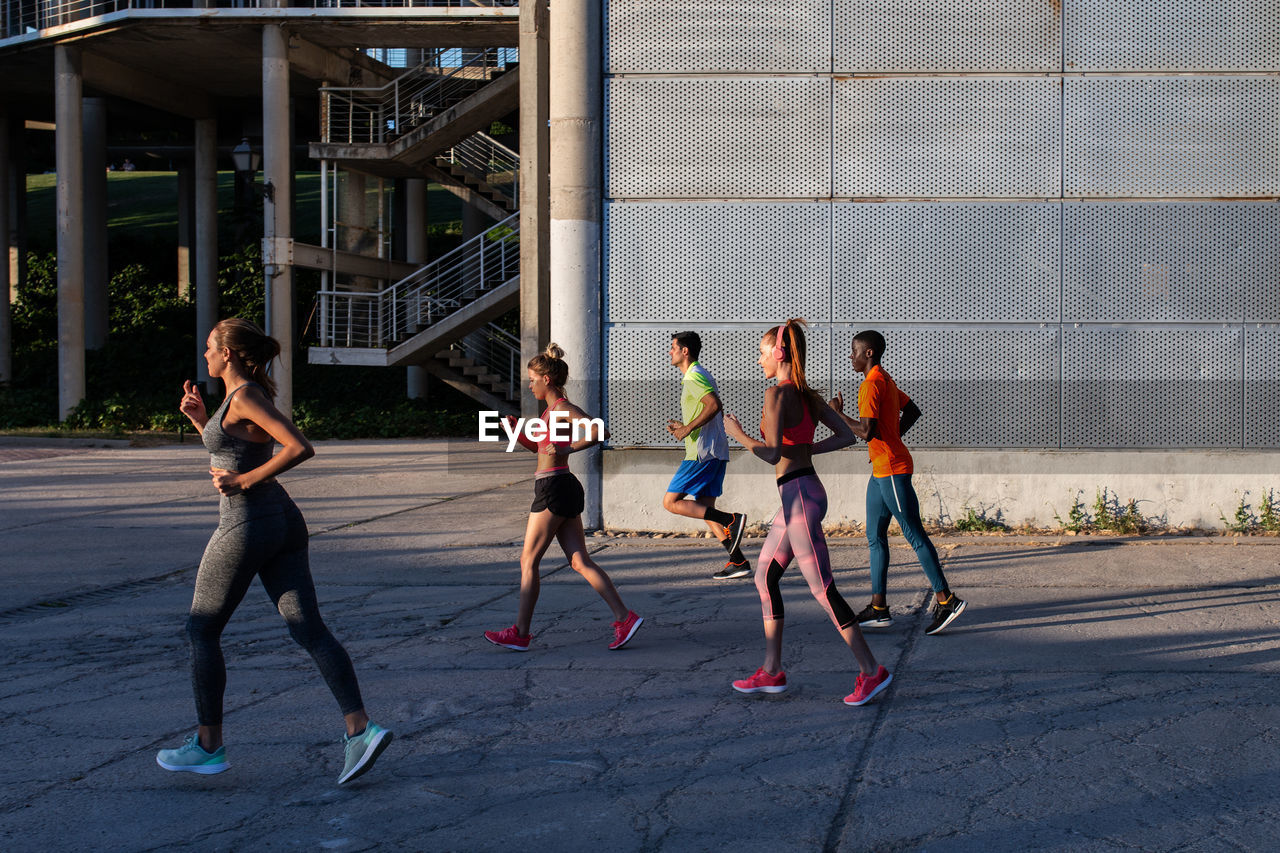 Side view of diverse sportspeople running along street while training together in city on sunny day