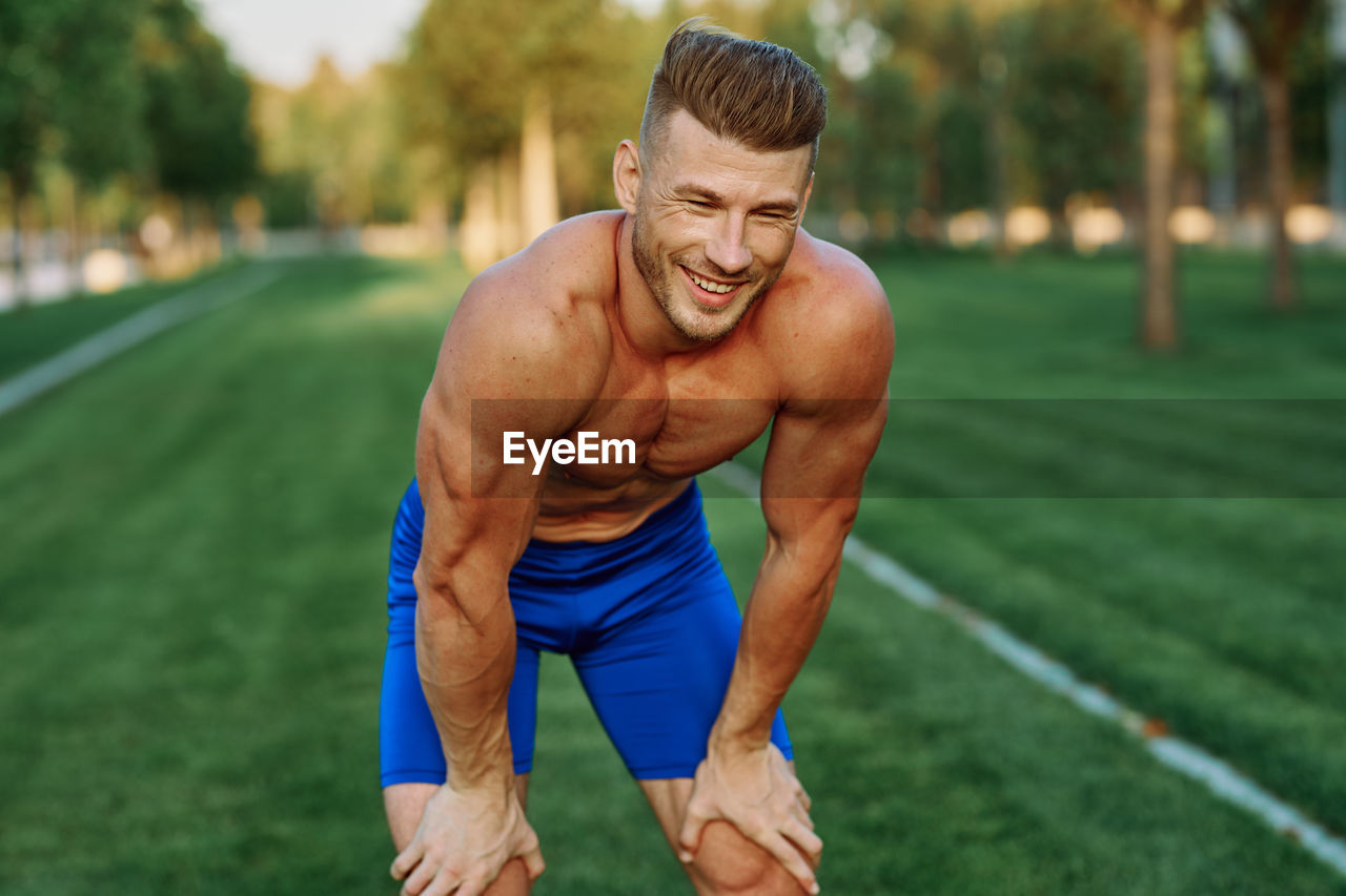 portrait of shirtless young man exercising on field