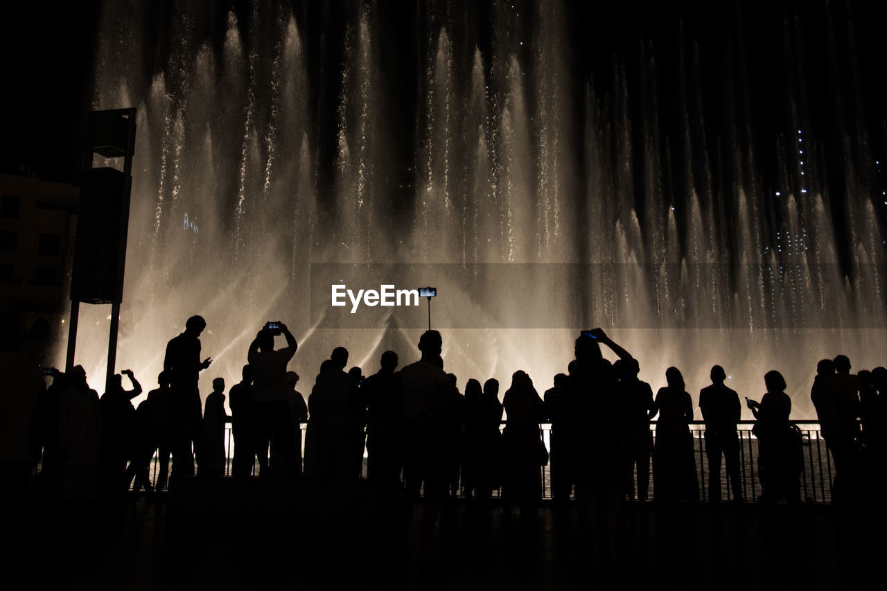 Silhouette people watching fountain show at night