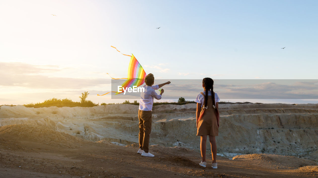 Children with a kite on a high rock near canyon in rays at sunset.