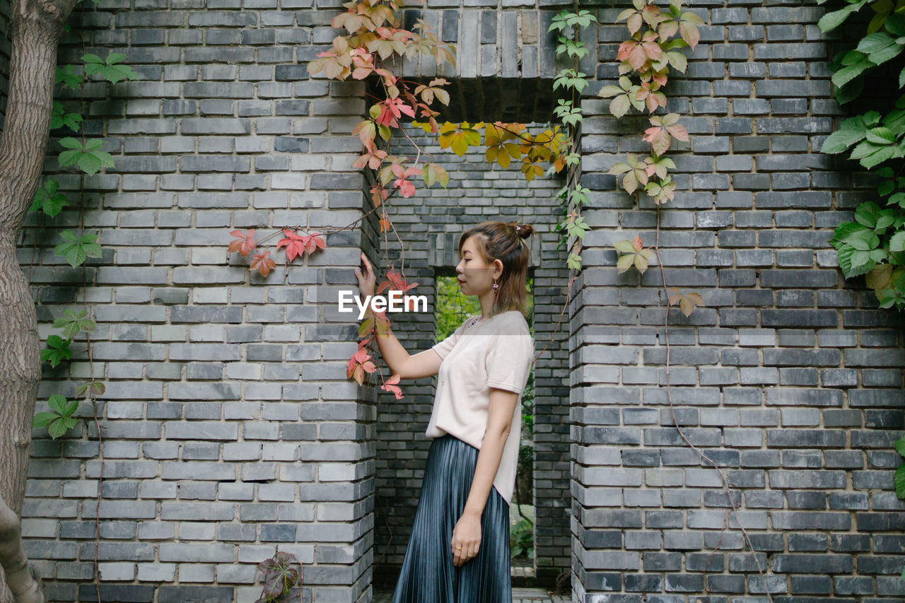 Full length of beautiful woman standing against brick wall