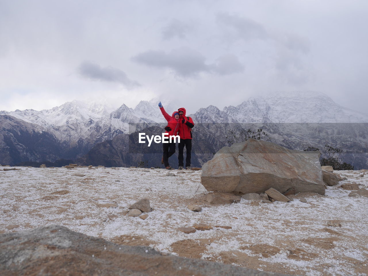 Couple with hand raised standing against snowcapped mountains