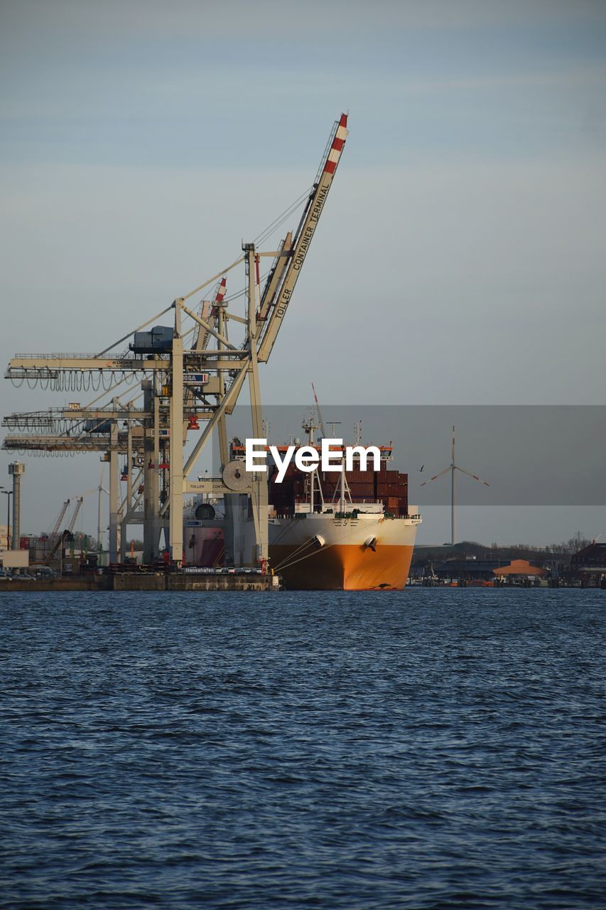 Cranes at commercial dock against sky