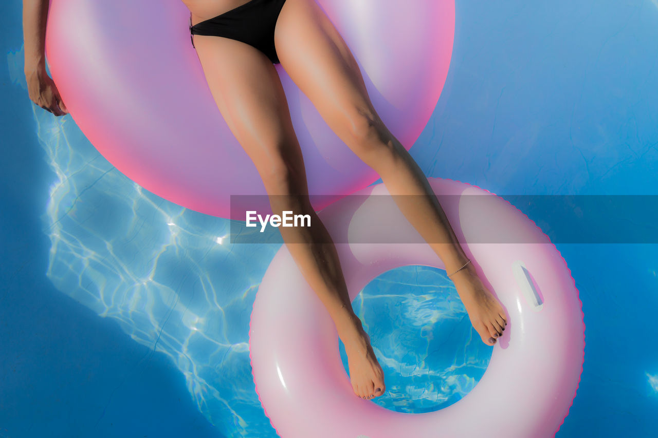 Lows section of woman relaxing on inflatable ring in swimming pool