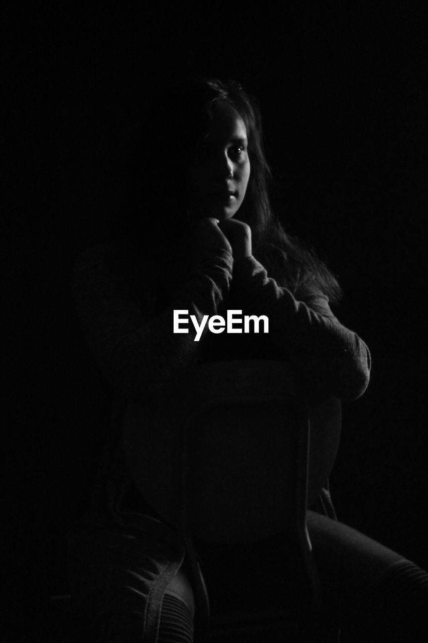 Thoughtful teenage girl sitting on chair in darkroom