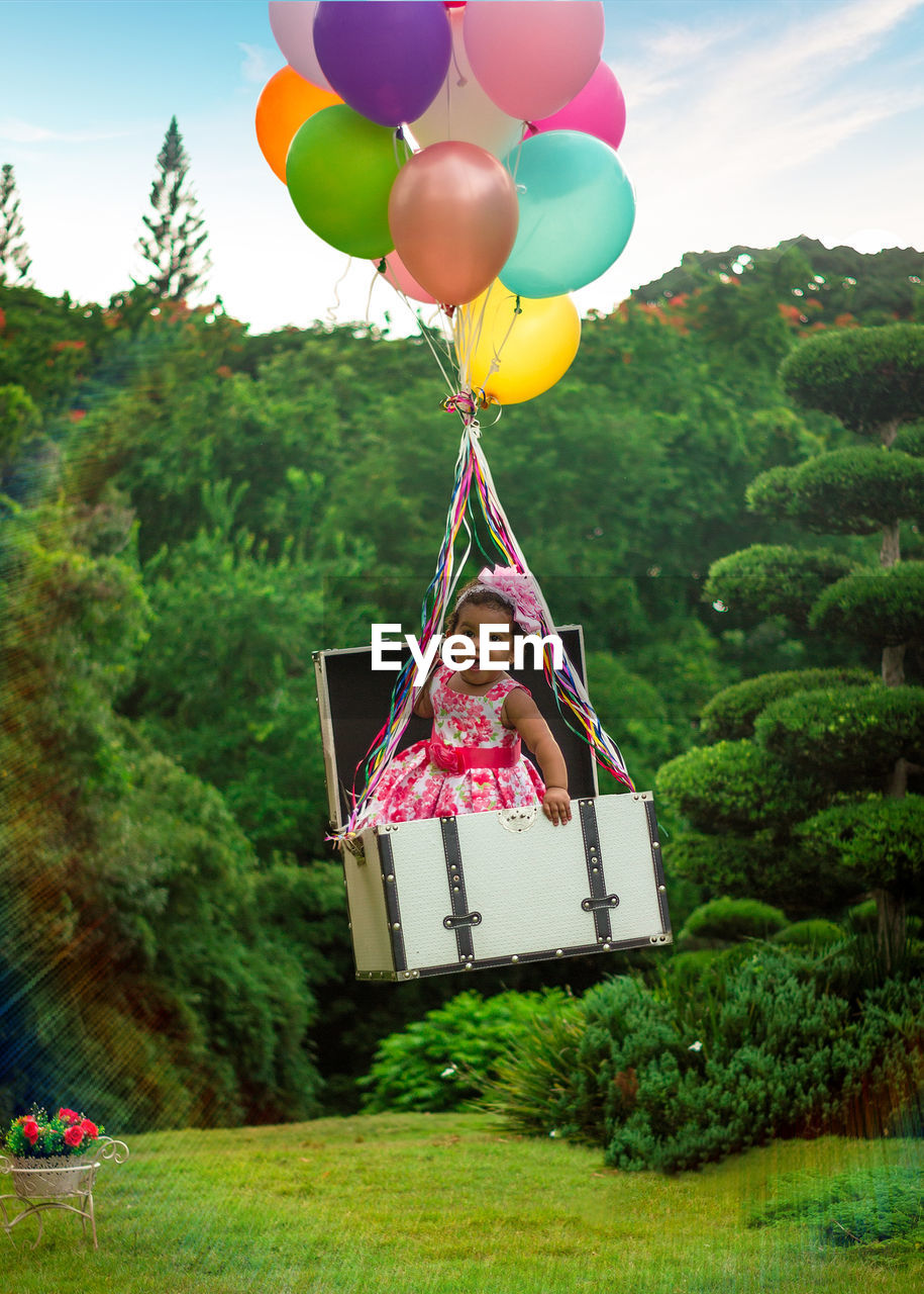 Portrait of cute girl in suitcase floating while tied to balloons