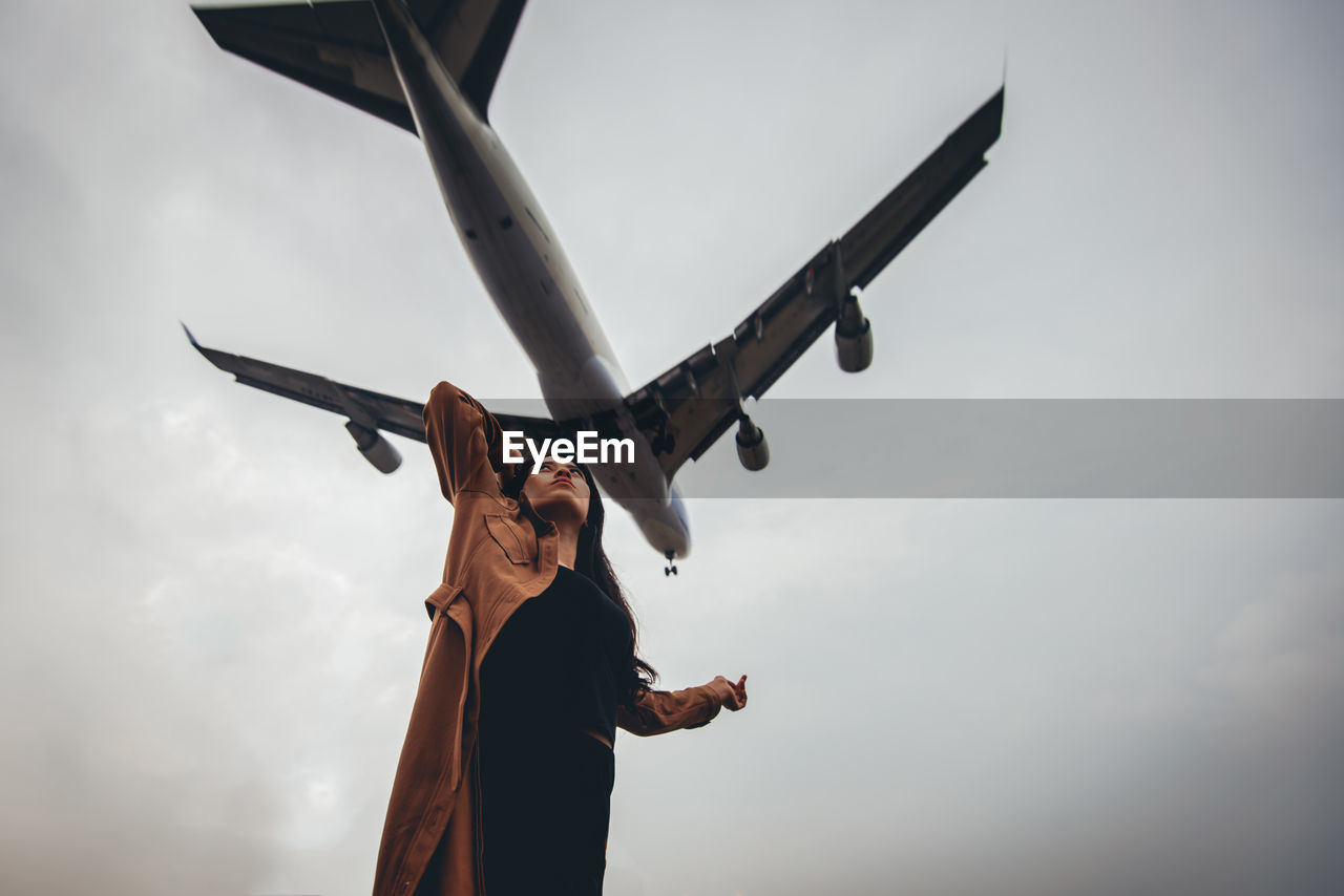 Airplane flying over woman against sky